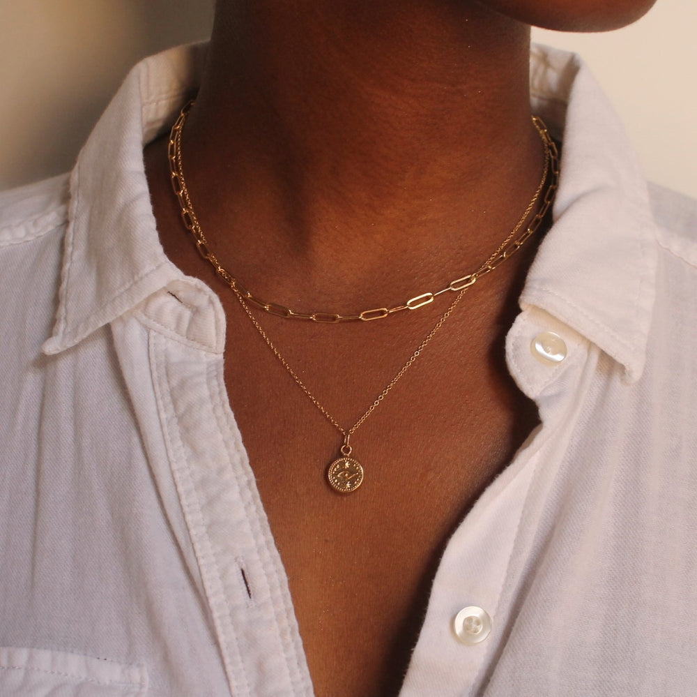 Model wearing gold elongated link and round evil eye necklaces